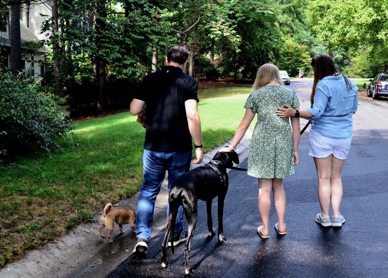 A mom, dad and their daughter walk down the street with a large black dog and small brown dog. The daughter was admitted to Brynn Marr hospital in 2022.